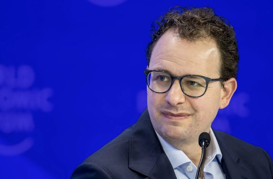 Мужчина в очках на фоне мероприятия, смотрит в сторону.