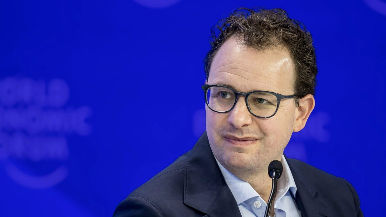 Мужчина в очках на фоне мероприятия, смотрит в сторону.