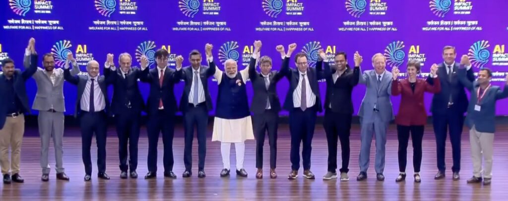 🇮🇳 Что реально произошло на India AI Impact Summit: цифры,... 1 Лидеры держатся за руки на сцене саммита AI Impact Summit 2023, фиолетовый задний фон.