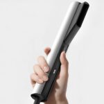 Рука держит черно-белый выпрямитель для волос на белом фоне.