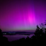 Северное сияние над озером ночью, фиолетовые и розовые оттенки в небе, вид на природу.