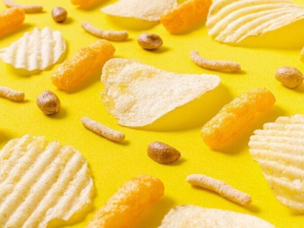 Чипсы, кукурузные палочки и орешки на желтом фоне, вид сверху.