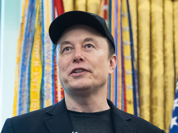 Человек в чёрной кепке на фоне декоративных флагов.