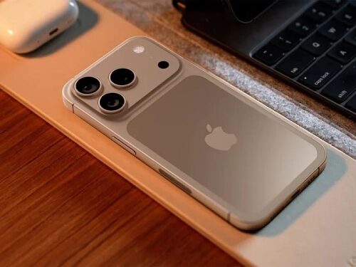 Современный смартфон с тройной камерой на рабочем столе рядом с клавиатурой и наушниками.