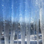 Сосульки на окне, морозное утро, голубое небо, вид через замерзшее стекло.