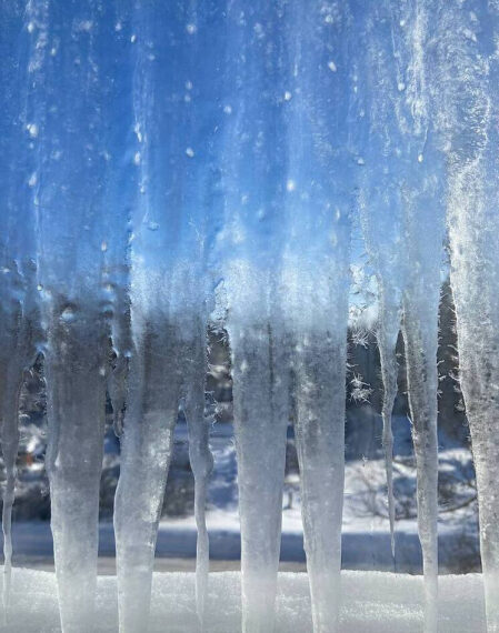 Сосульки на окне, морозное утро, голубое небо, вид через замерзшее стекло.