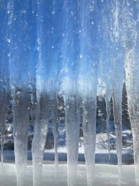 Сосульки на окне, морозное утро, голубое небо, вид через замерзшее стекло.