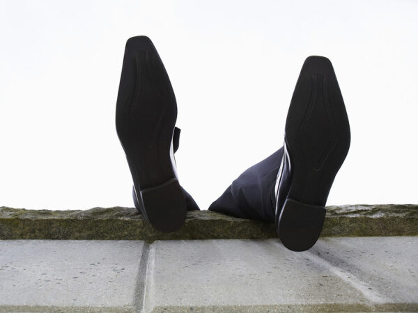 Мужчина в костюме лежит на стене, видны только его ноги в черных туфлях на фоне неба.