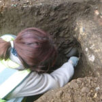 Археолог за работой, исследует раскоп в грунте.