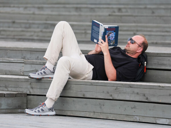 Мужчина лежит на деревянных ступенях и читает книгу на свежем воздухе.