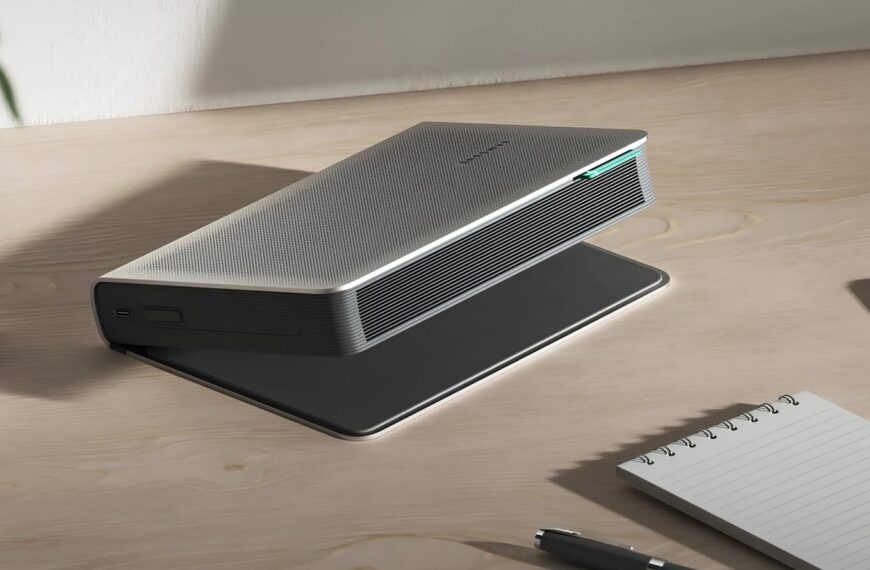 Современный проектор на столе рядом с блокнотом и ручкой.