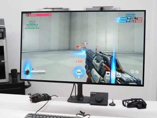 Компьютерный монитор с видеоигрой на столе, клавиатура и контроллер рядом.