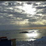 Антарктика: облака над морем и льдинами, закатное солнце отражается в воде.