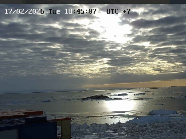 Антарктика: облака над морем и льдинами, закатное солнце отражается в воде.