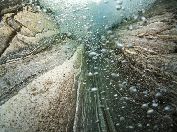 Подводный вид из ущелья с пузырьками воздуха и слоистыми камнями.