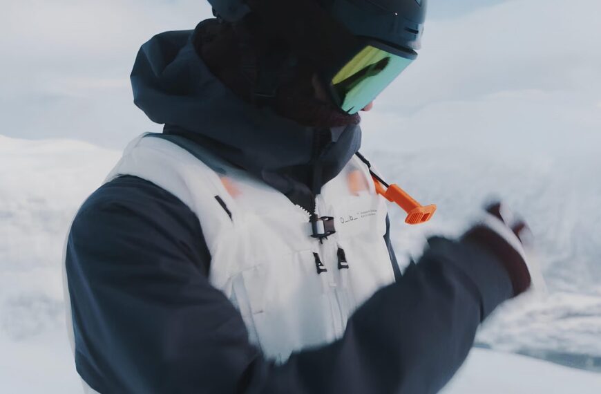 Человек в снегу в зимней одежде, в шлеме и очках, с оранжевым сигналом.