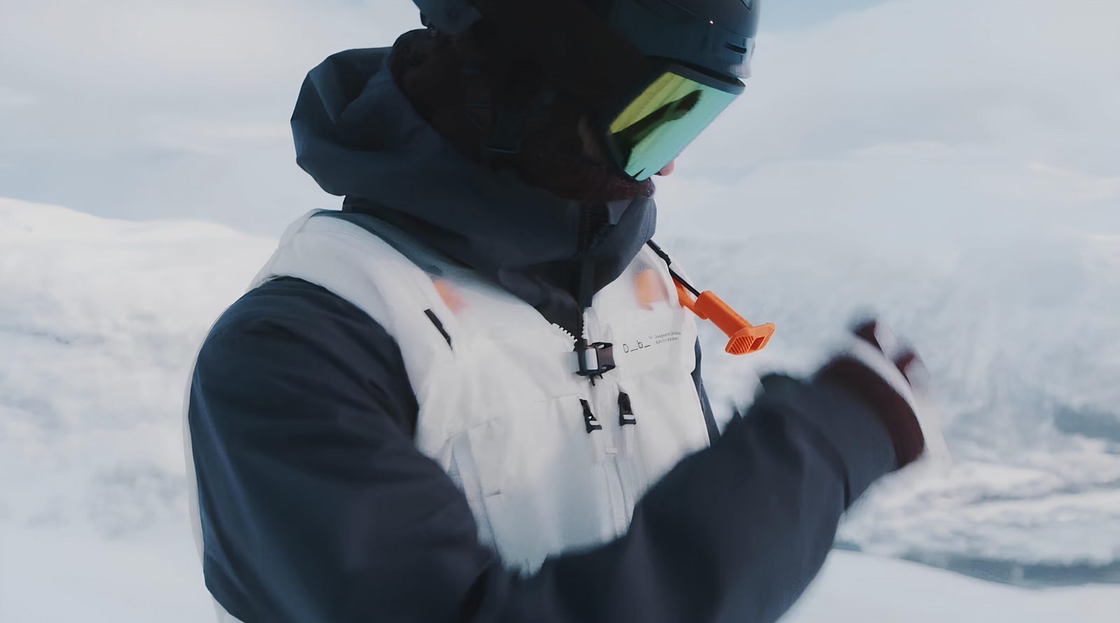 Человек в снегу в зимней одежде, в шлеме и очках, с оранжевым сигналом.