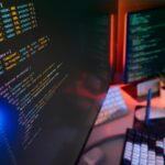 Код на экране компьютера в офисе программиста, клавиатура, мышь и растение на столе.