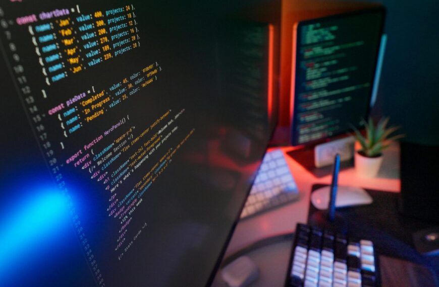 Код на экране компьютера в офисе программиста, клавиатура, мышь и растение на столе.