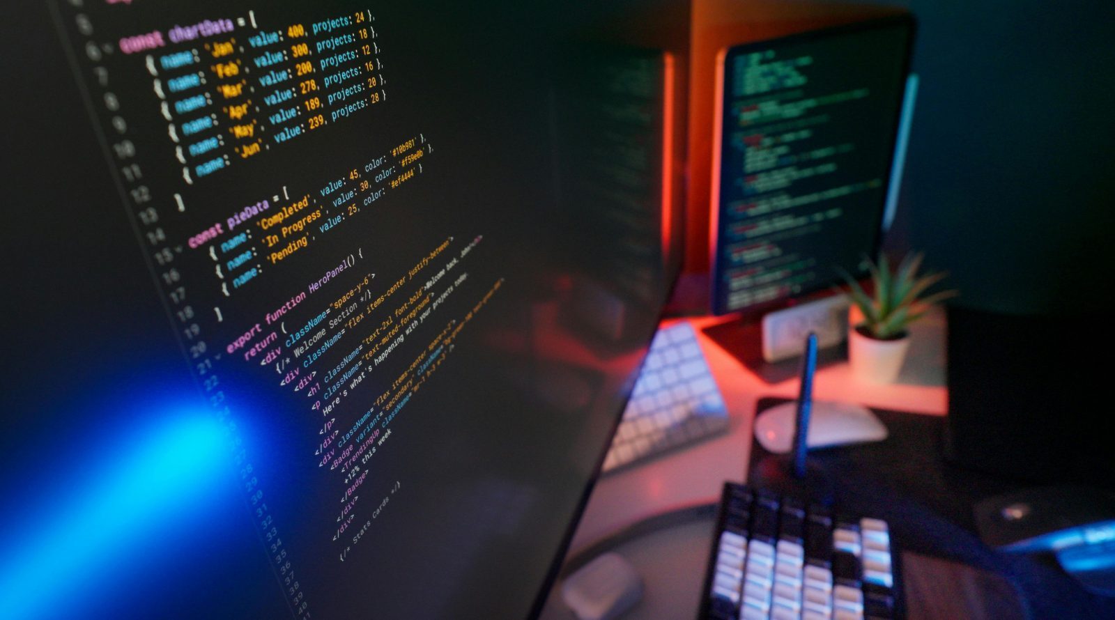 Код на экране компьютера в офисе программиста, клавиатура, мышь и растение на столе.