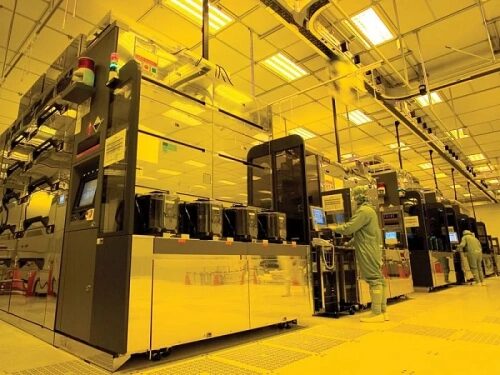 Чистая комната полупроводникового завода с оборудованием и сотрудниками в защитной одежде.