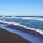 Пляж с черным песком и волнами на фоне ясного неба.