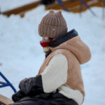 Человек в теплой одежде на улице зимой, сидит на лавке в шапке и шарфе.