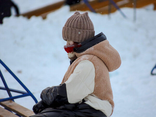 Человек в теплой одежде на улице зимой, сидит на лавке в шапке и шарфе.