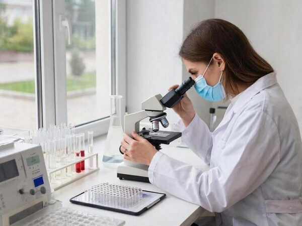 Учёные открыли ген, ухудшающий настроение зимой 3 Женщина в лаборатории изучает образцы под микроскопом, носит маску и халат.