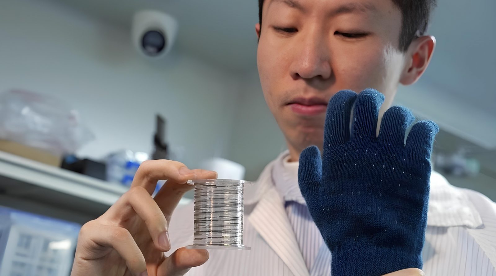 Учёные создали электронное волокно для «умной» одежды и медицины 2 Человек в лаборатории держит катушку с тонкой проволокой в руке в синей перчатке.