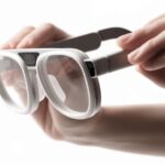 Руки держат белые стильные очки с толстыми рамками на белом фоне.