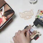Сборка машинки с помощью паяльника и подсказок через смартфон на деревянной подставке.