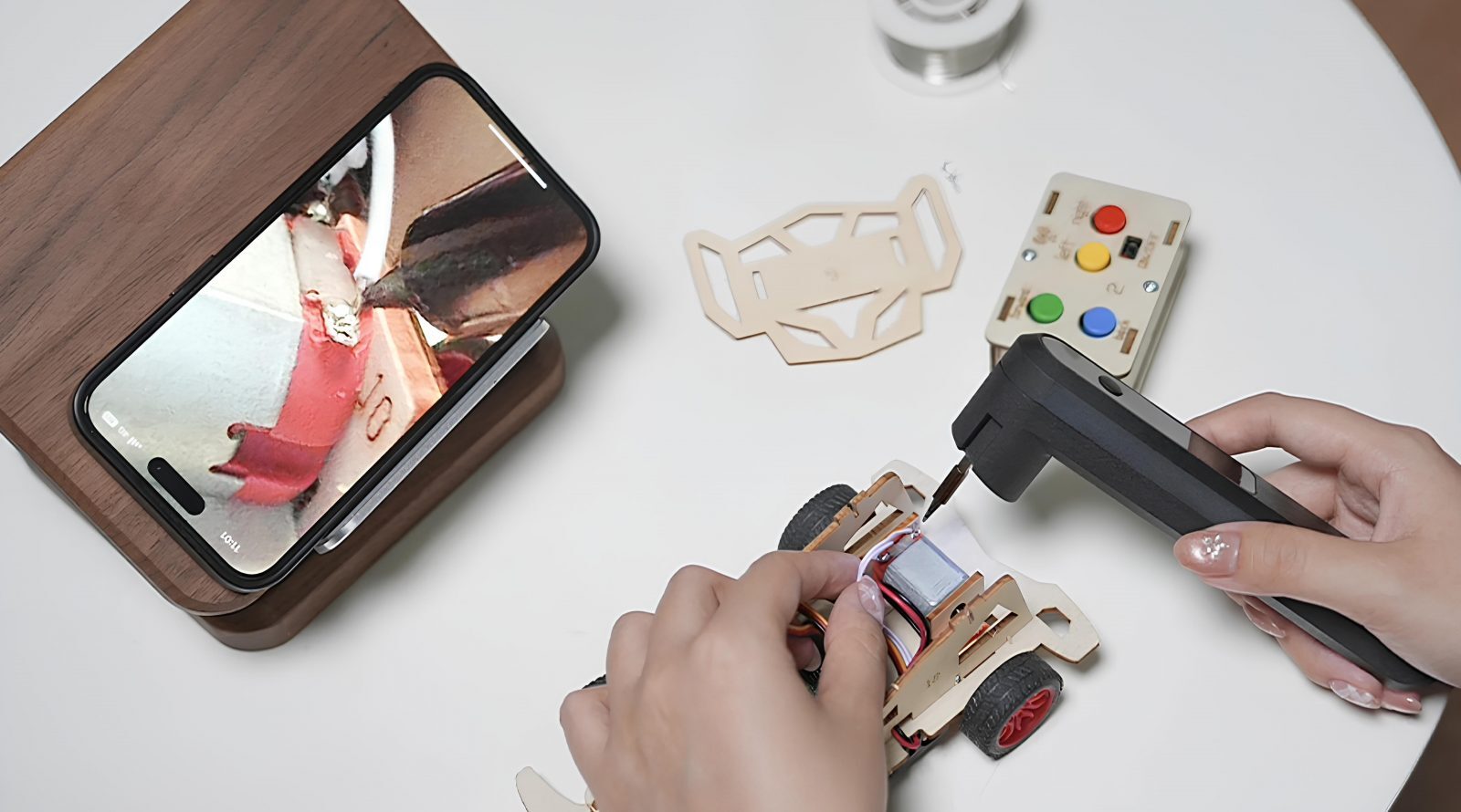 Сборка машинки с помощью паяльника и подсказок через смартфон на деревянной подставке.