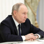 Мужчина в костюме сидит за столом с бумагами, внутренний интерьер офиса.