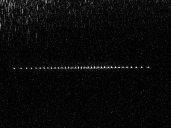 Темное небо с яркой линией звезд, похожих на спутники, на фоне.