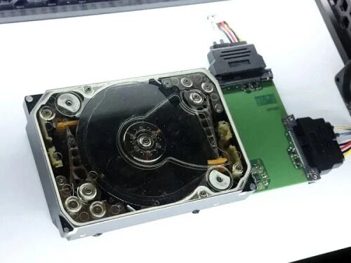 Старый жёсткий диск с прозрачной крышкой, разобранный для показа внутренней структуры.