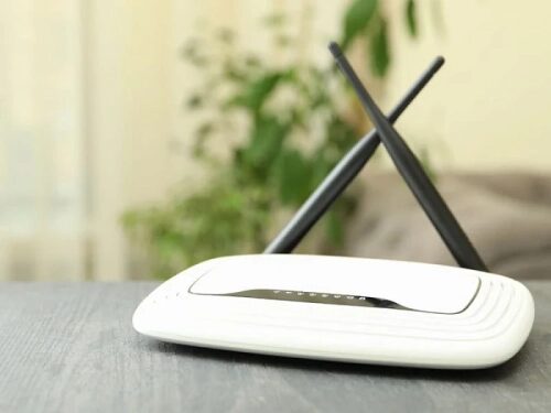 Белый Wi-Fi роутер с двумя антеннами на столе, растение на фоне.