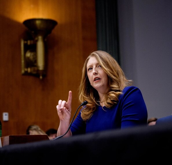 Женщина говорит на собрании, указывая вверх, микрофон на столе.