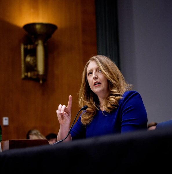 Женщина говорит на собрании, указывая вверх, микрофон на столе.