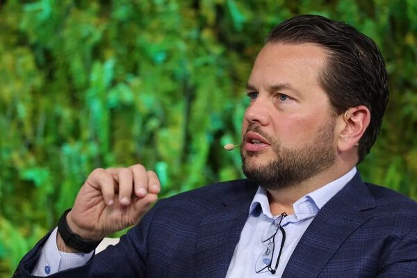 Мужчина в костюме на конференции с микрофоном, зеленый фон из растений.