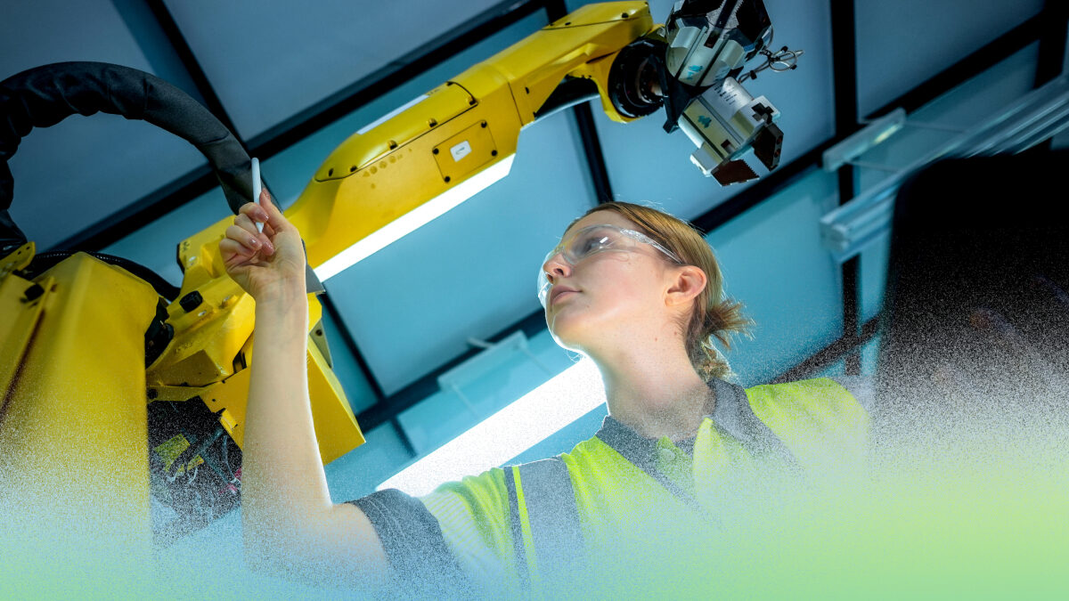 Человек работает с промышленным роботом на производстве, проверяя оборудование.