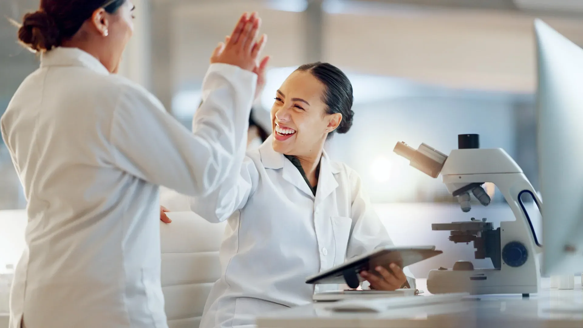 Два ученых в лаборатории обсуждают результаты перед микроскопом.