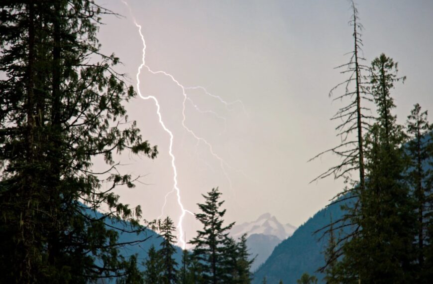 Гроза в горах: молния сверкает среди деревьев и горных вершин.