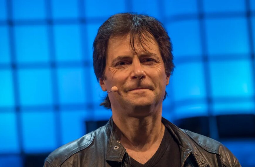 Мужчина в кожаной куртке на фоне синего экрана на конференции или презентации.