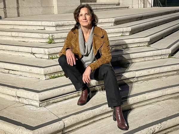 Женщина с каштановыми волосами сидит на каменных ступенях.