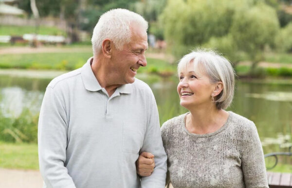 Пожилая пара улыбается и гуляет на природе у озера.