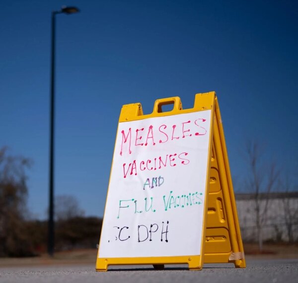 Табличка с информацией о вакцинах от кори и гриппа на улице.