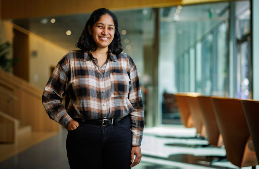 Человек в клетчатой рубашке стоит в современном офисе.