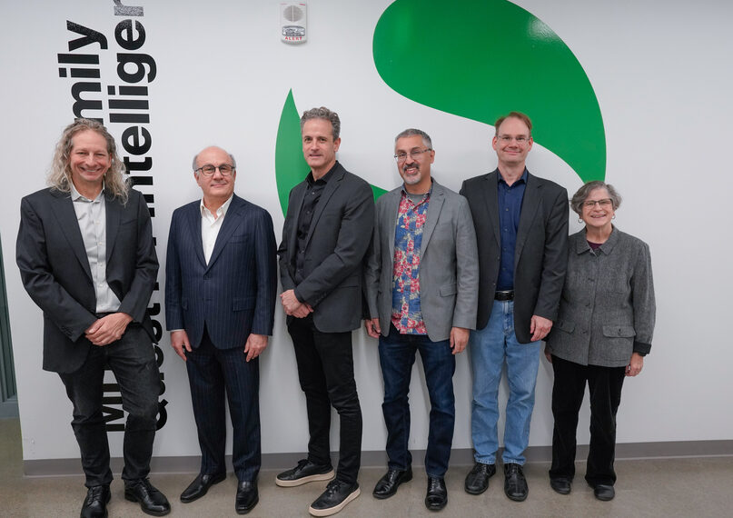 Группа людей на фоне логотипа компании, одеты в деловую одежду.