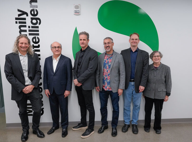 Группа людей на фоне логотипа компании, одеты в деловую одежду.